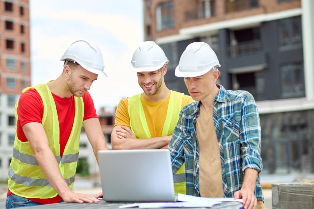 important-information-three-men-protective-helmet-looking-laptop-with-interest-while-standing-construction-site-day